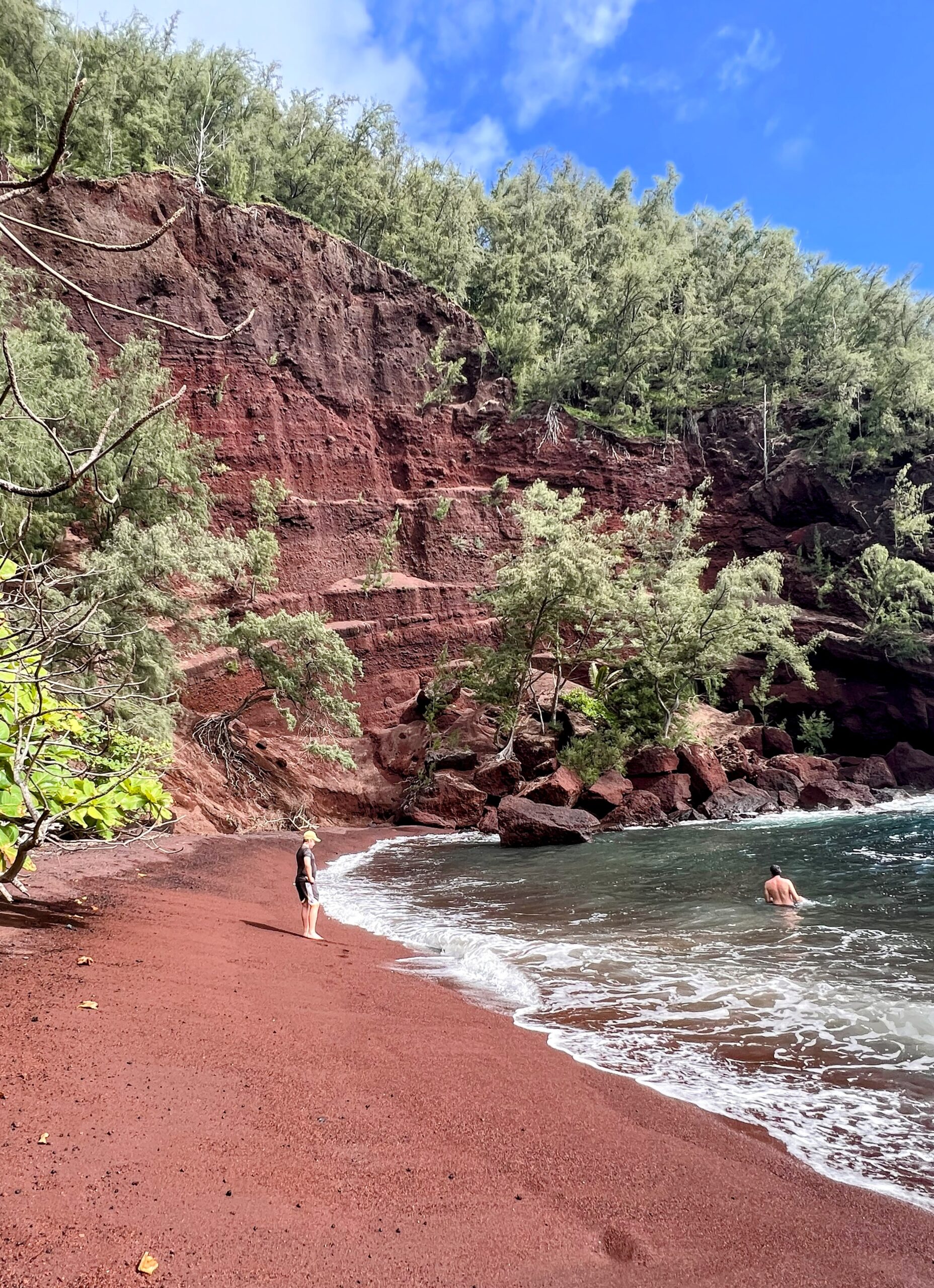 red sand beach with swimmers on Maui's east cost with tall red rock cliffs behind the beach