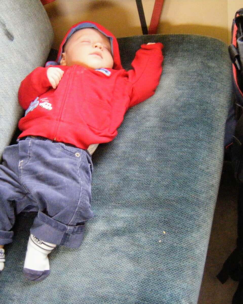 baby stretched out on a seat and sleeping whilst travelling on an old train in norway