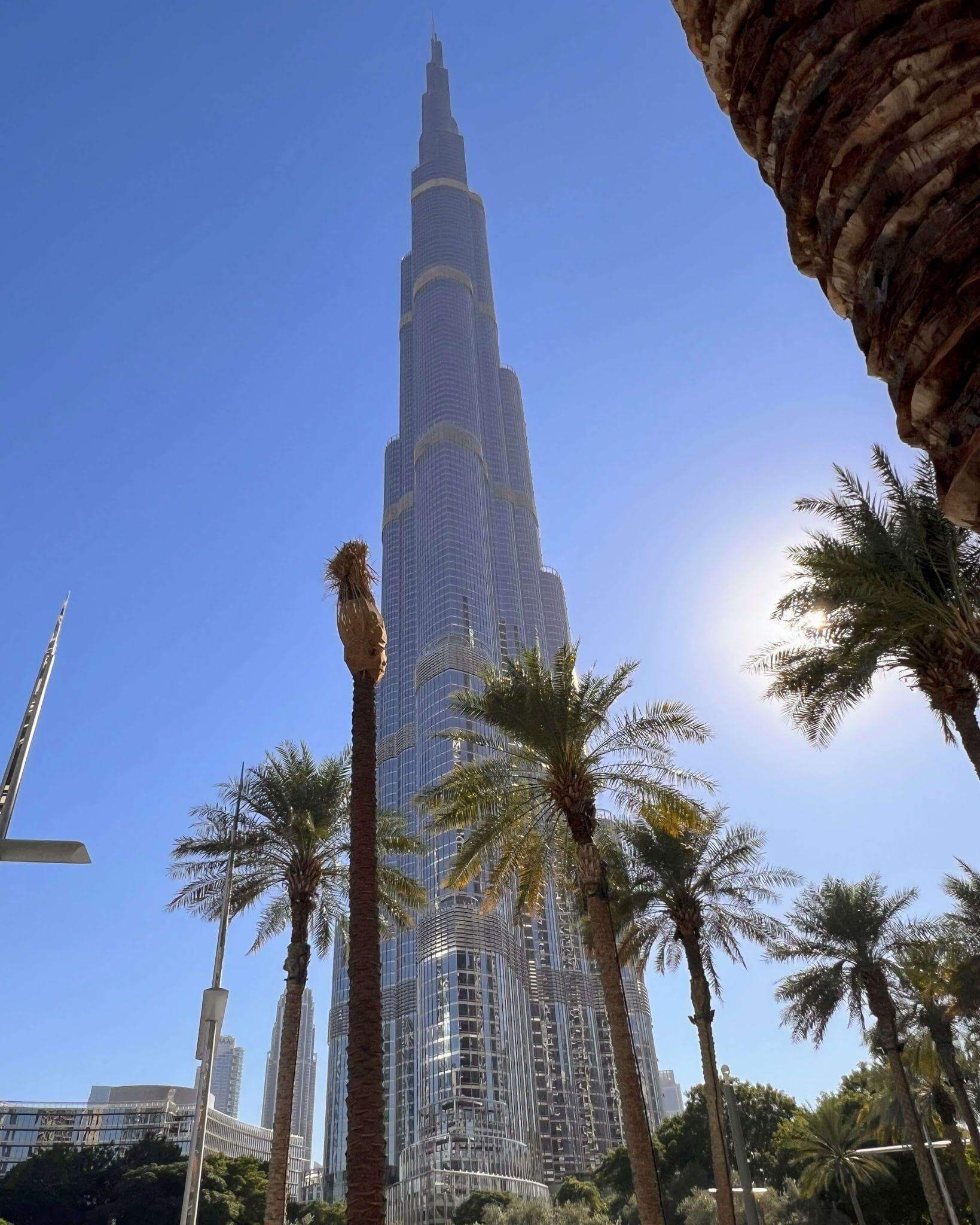 Burj Kalifa tower in Dubai towering into the blue sky with palm trees in the foreground
