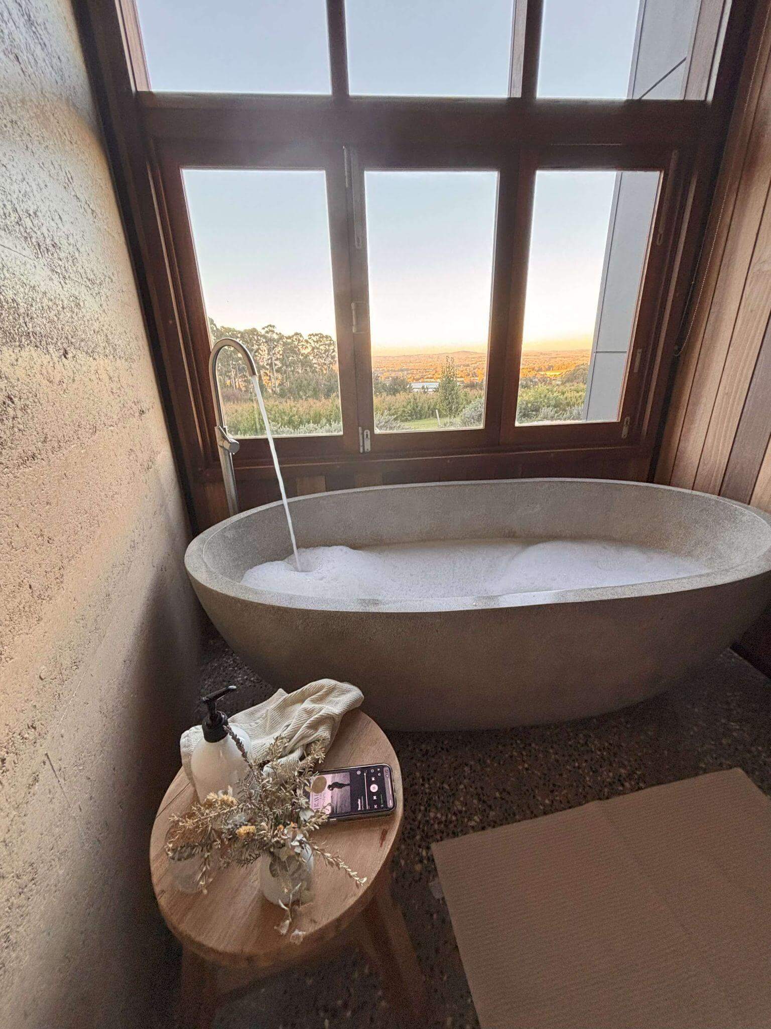 concrete oval bubble bath being filled with warm water in a boutique hotel with lovely country views outside