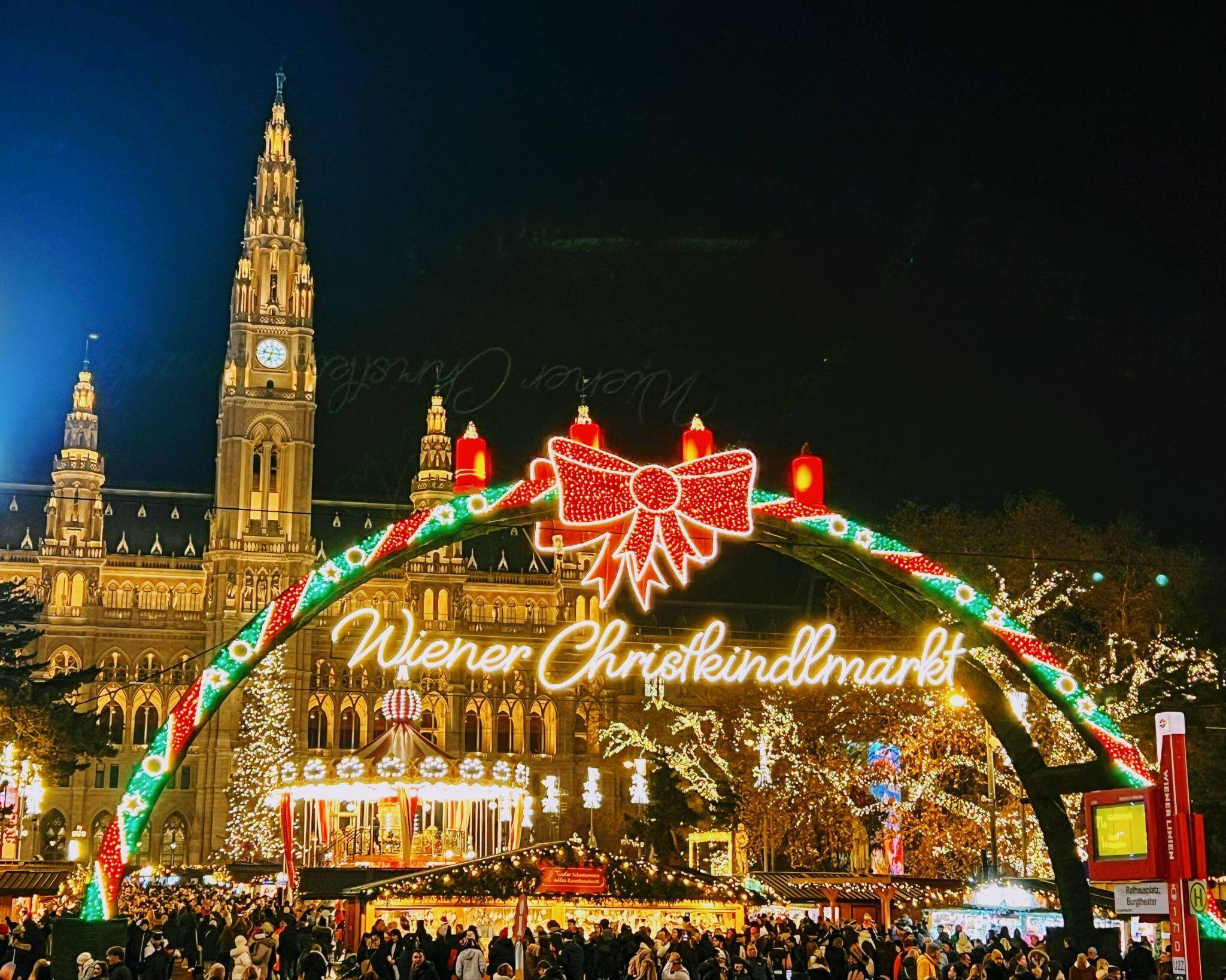entrance to the christmas markets in vienna with the parliament building in the background, lots of christmas lights, stalls and crowds of people