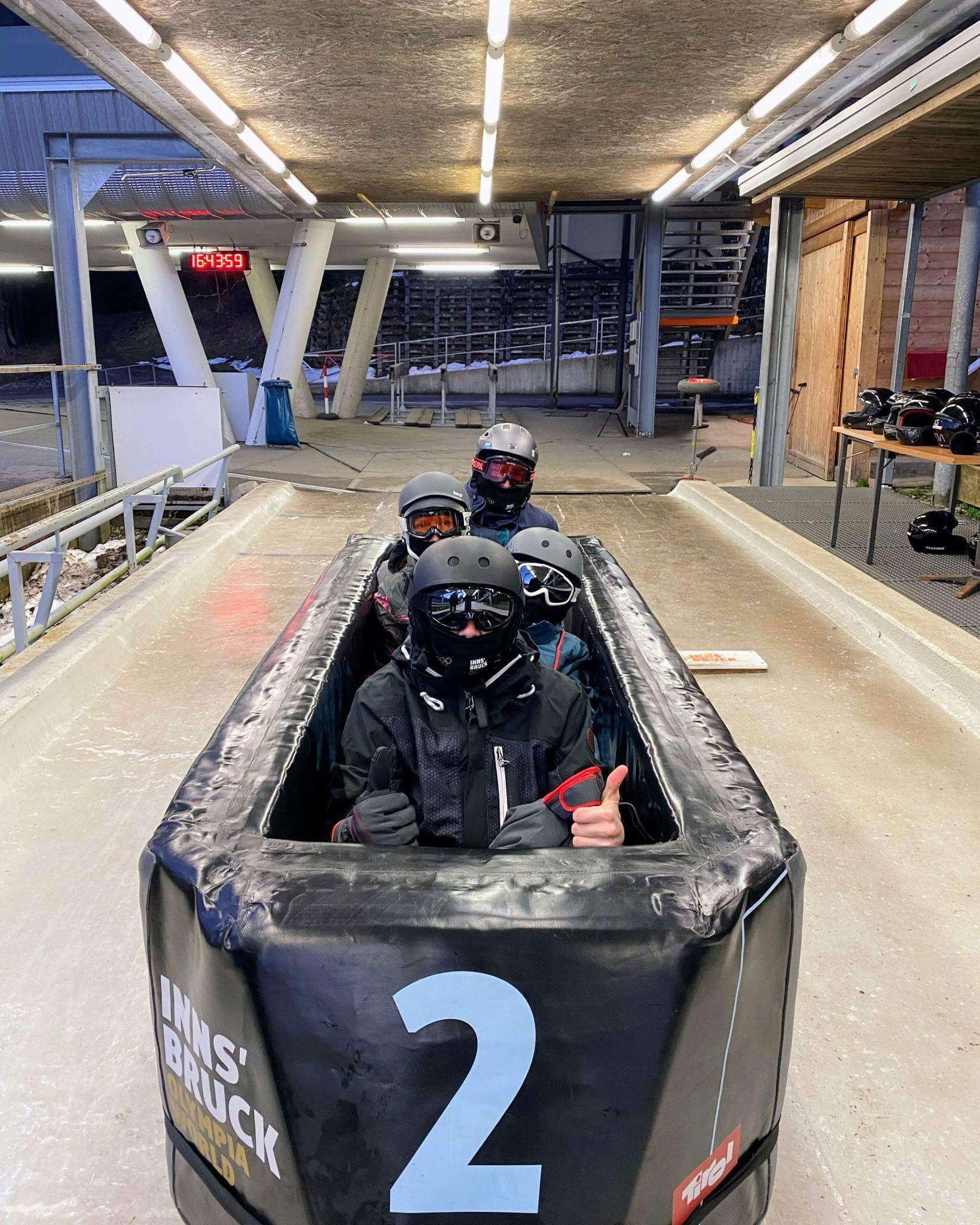Family getting ready to bobsled in Innsbruck, Austria, wearing helmets and ski goggles and sitting in a padded bobsled on the ice track