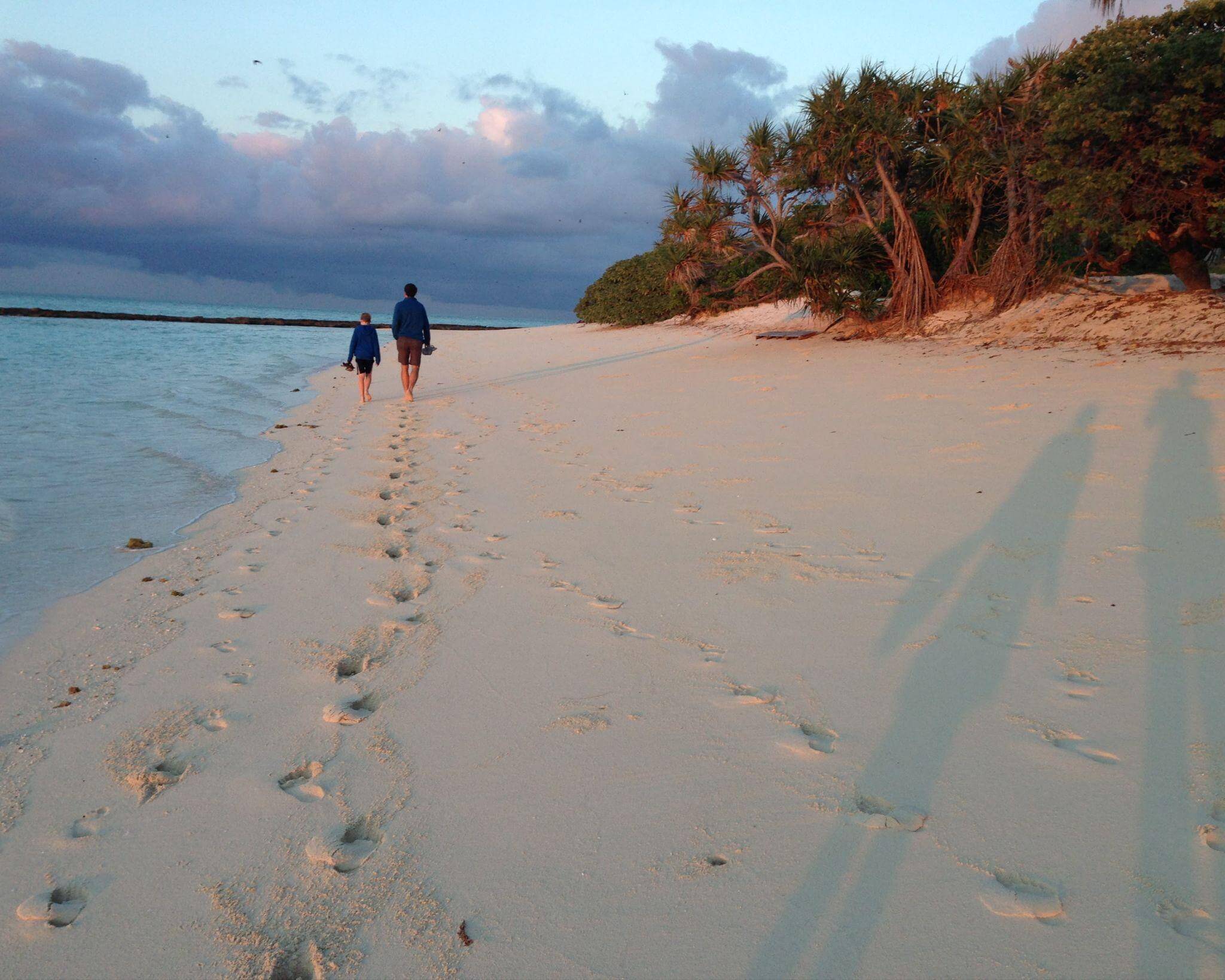 Father and son walking down the white sandy beach of Heron Island, Queensland in the early morning light and crystal clear ocean waters