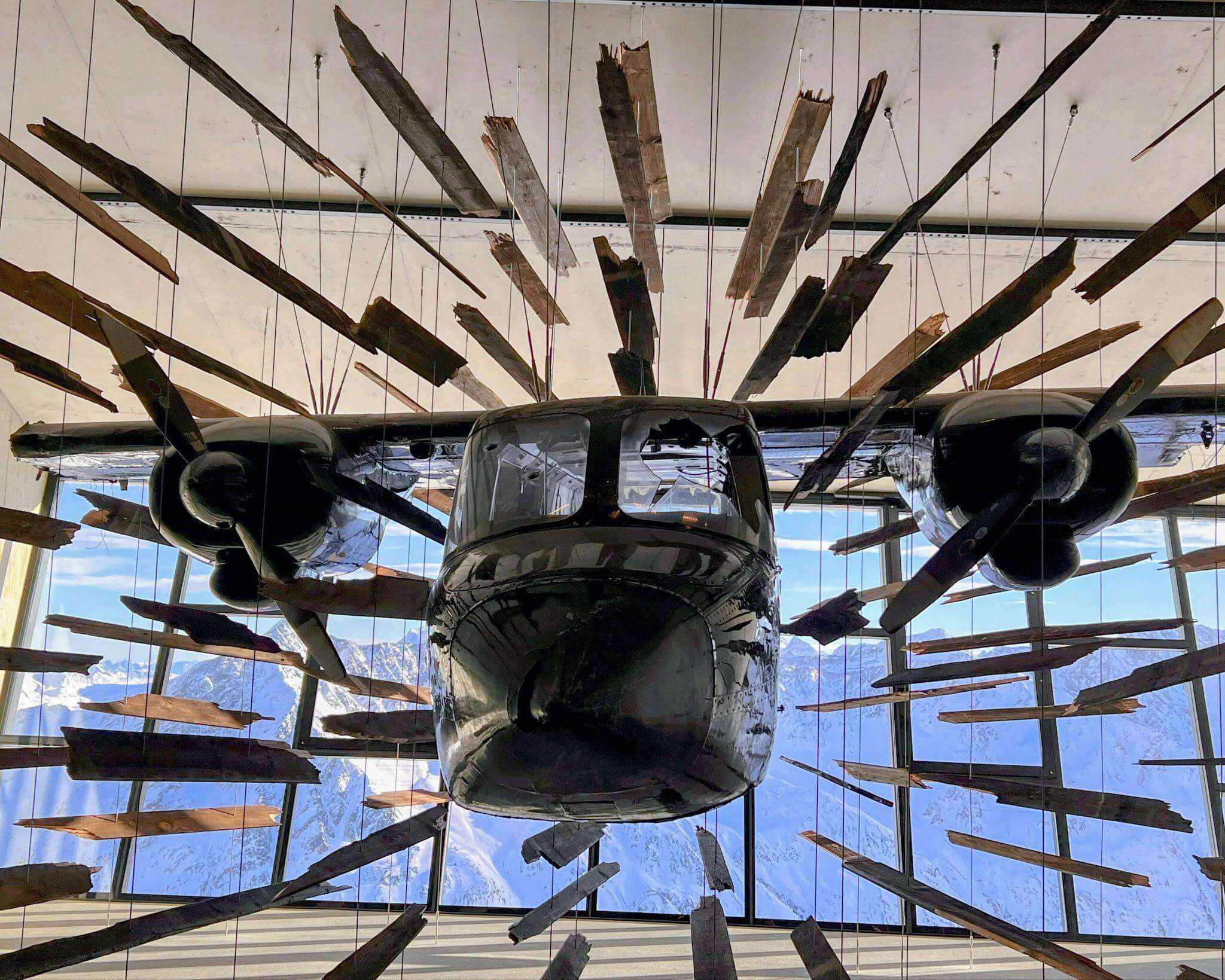 museum of artifacts used in james bond movie including a recreation of a plan bursting through a wooden building with the austrian alps visible through the glass wall of the museum