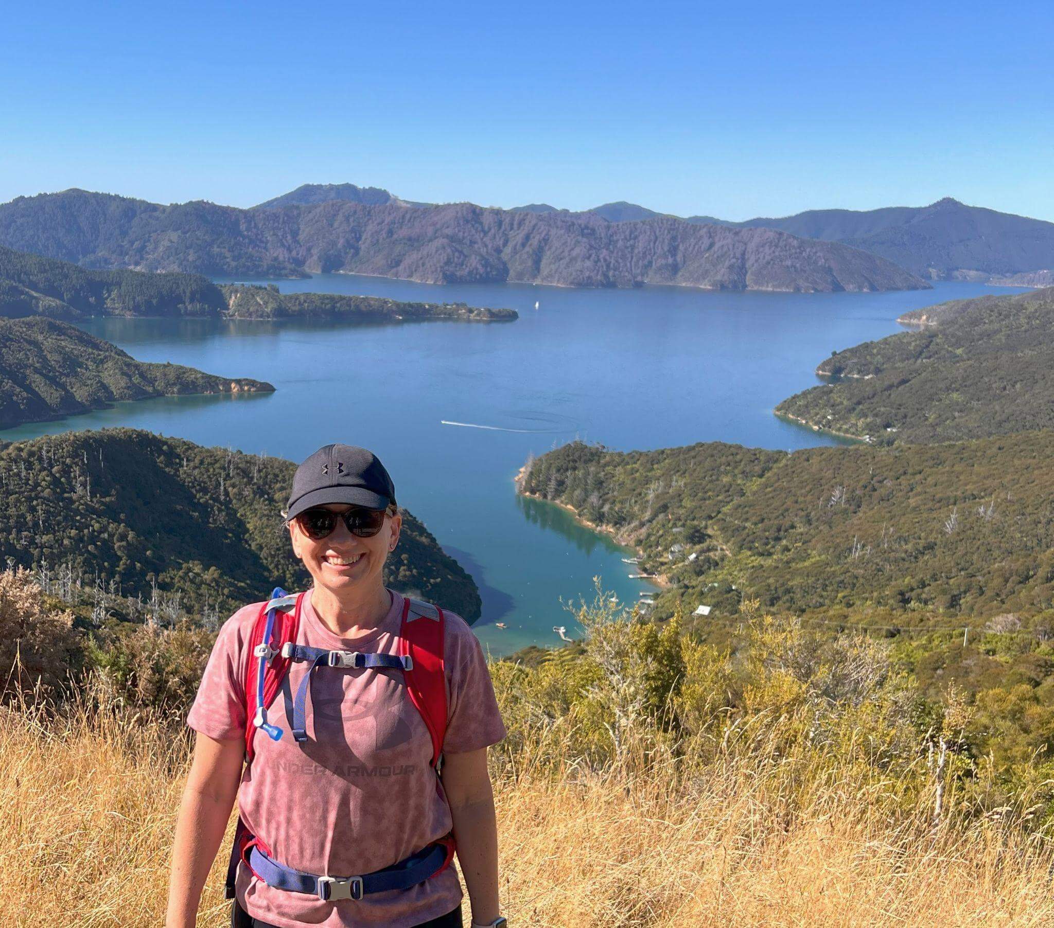 Rachel Reinke hiking the Queen Charlotte track with stunning panoramic view of QUeen Charlotte sound in the background