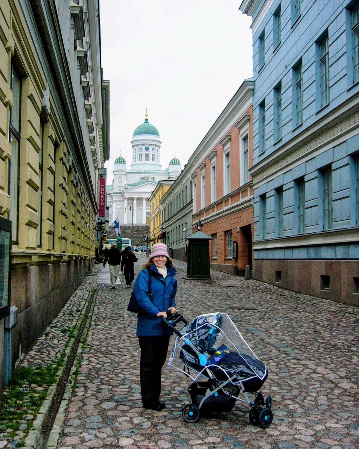 Rachel Reinke pushing a baby in a stroller along narrow cobbled street in Helsinki with a church in the background
