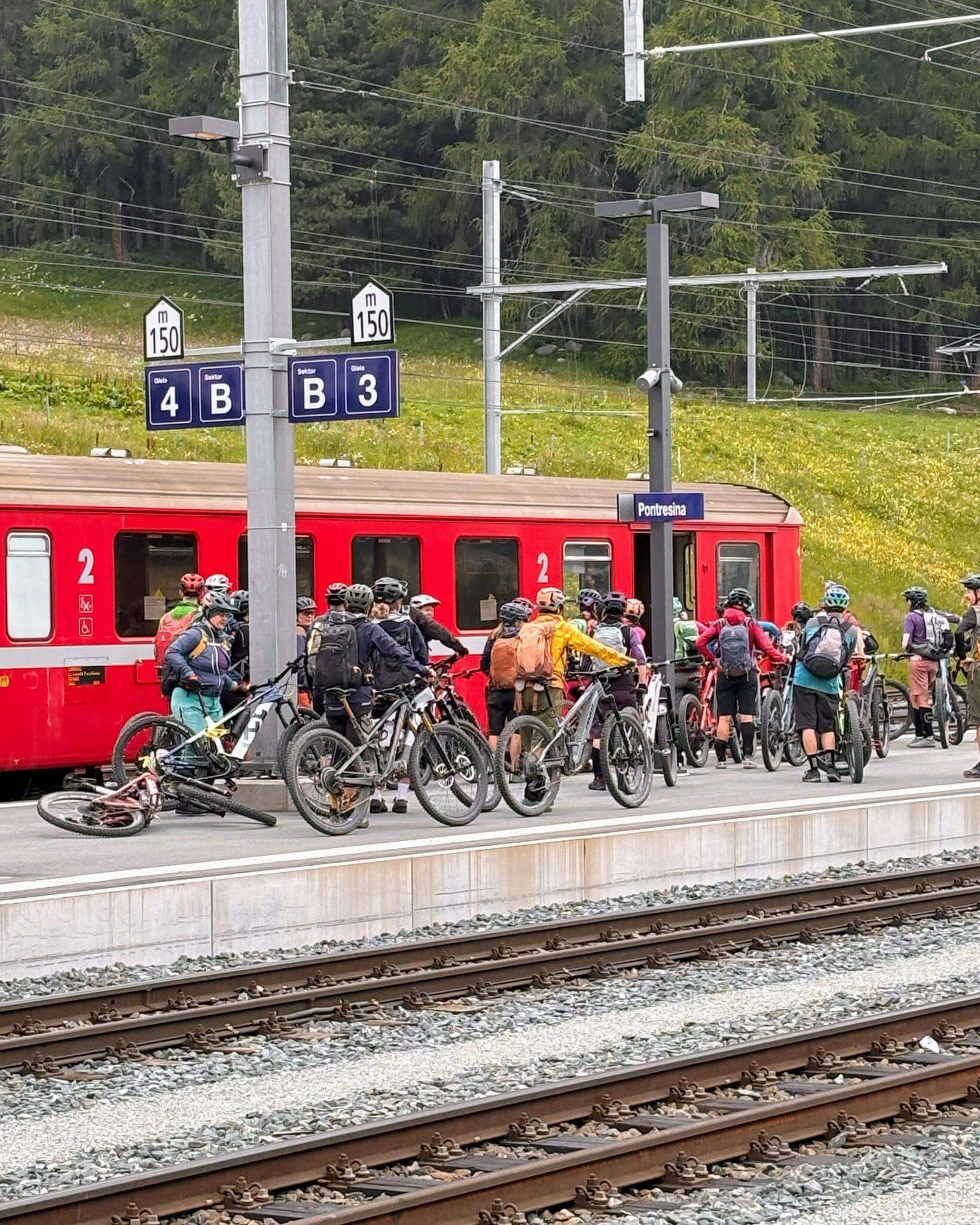 Two dozen cyclists with bicycles on a platform in pontresina switzerland ready to board a single carriage on a red train