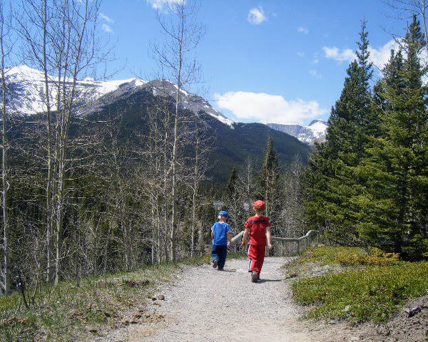 Two young children hiking on a path through the pine tree forest in canada with snow capped mountains in the background