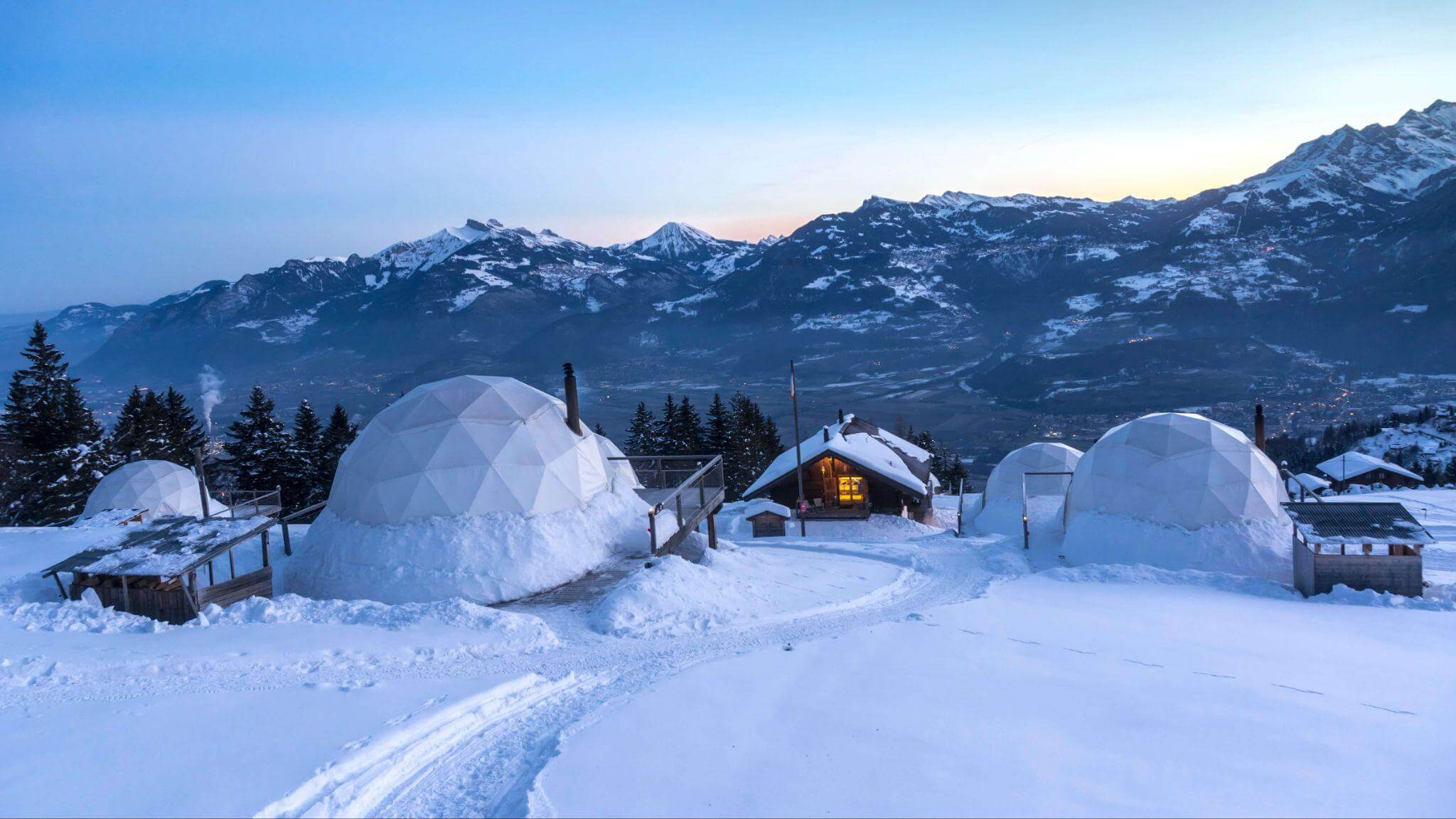 unique dome shaped igloo accommodation village in the thick now with snow covered mountains in the background