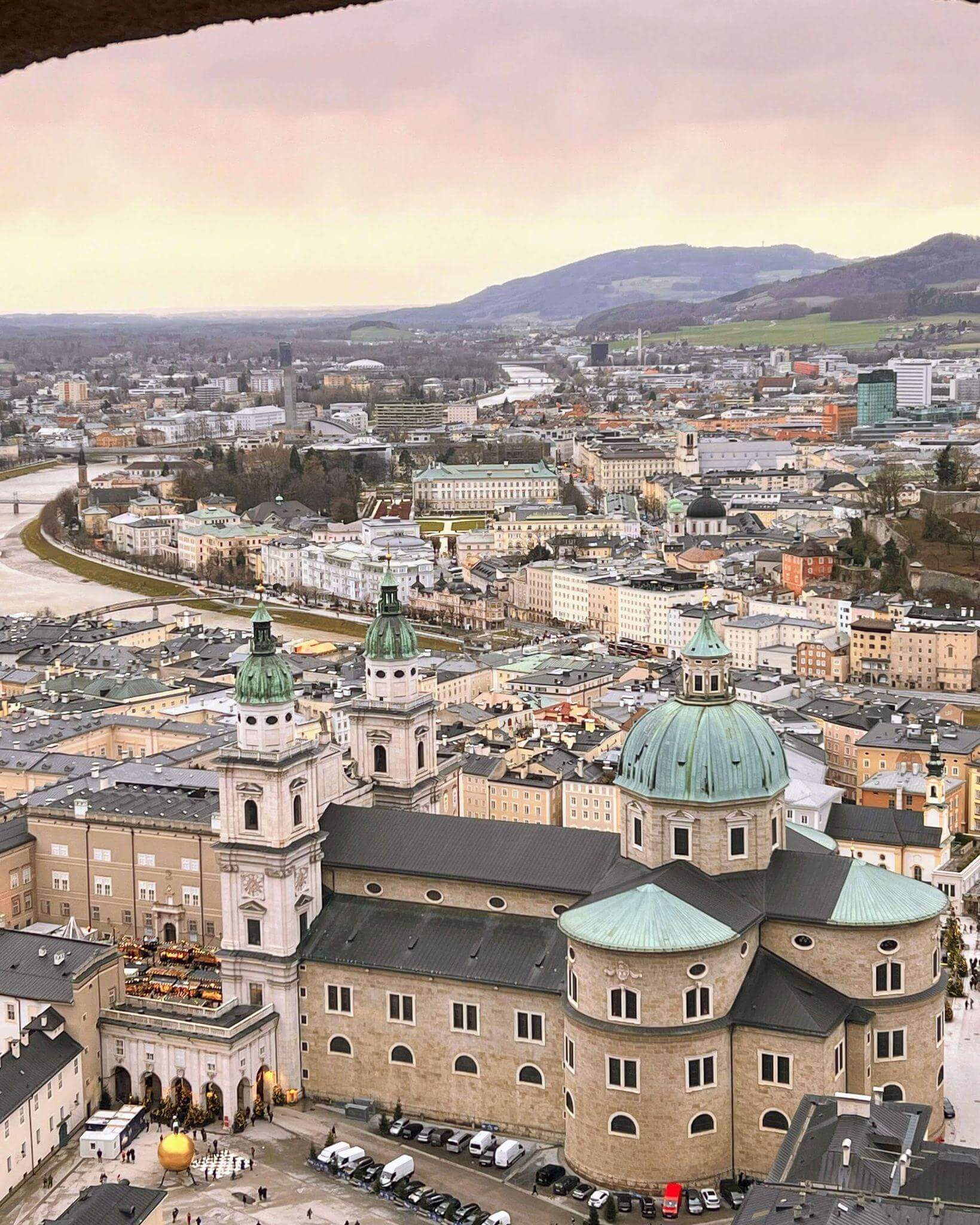 view from inside salzburg fortress over the city with the cathedral in the foreground, the salzach river and city buildings and hills in the background
