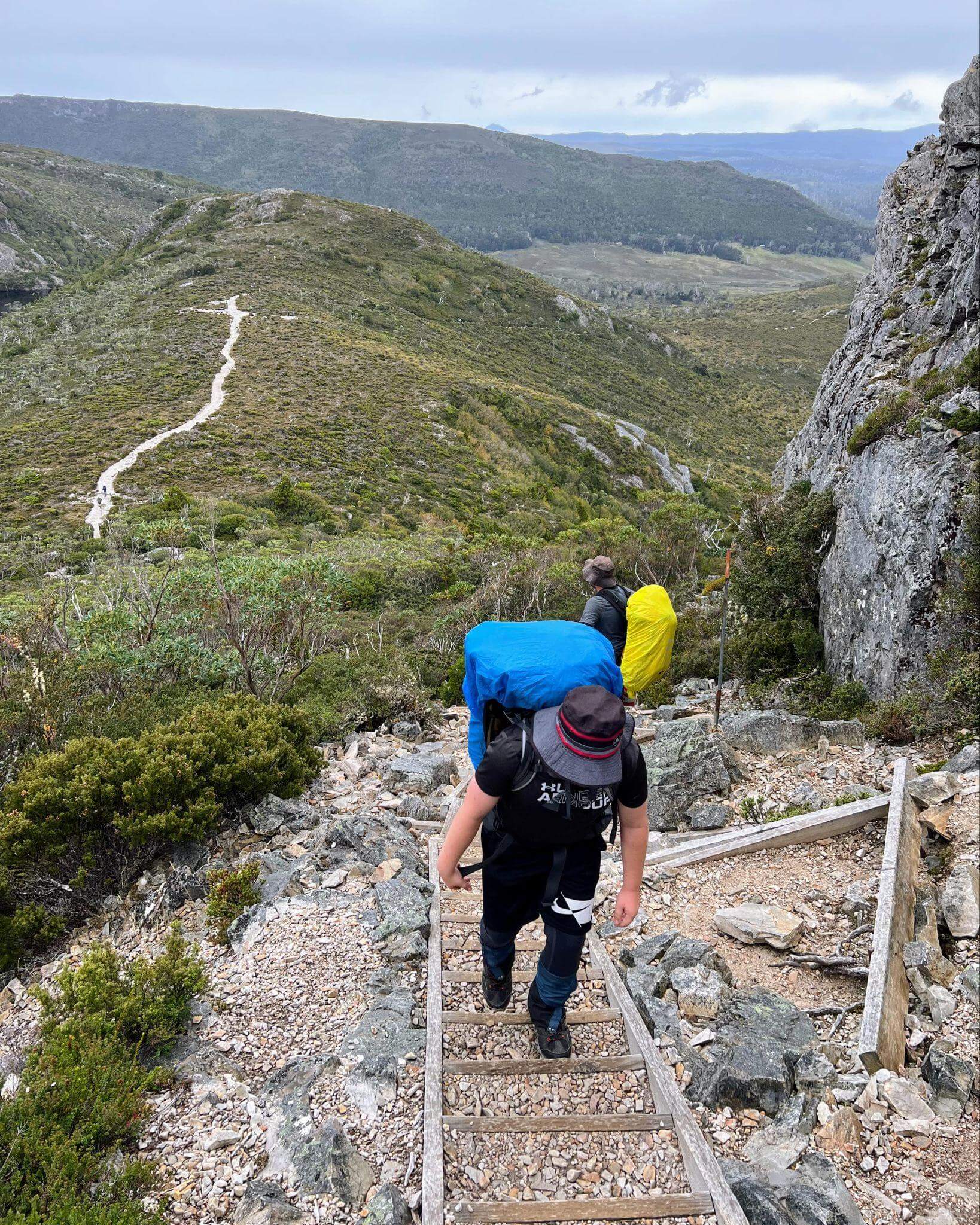Hikers with heavy packs ascending rocky terrain to marions lookout on the overland track