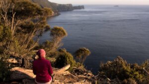 Rachel Reinke looking out over an expansive ocean at sunset from a high lookout point with cape pillar in the distance