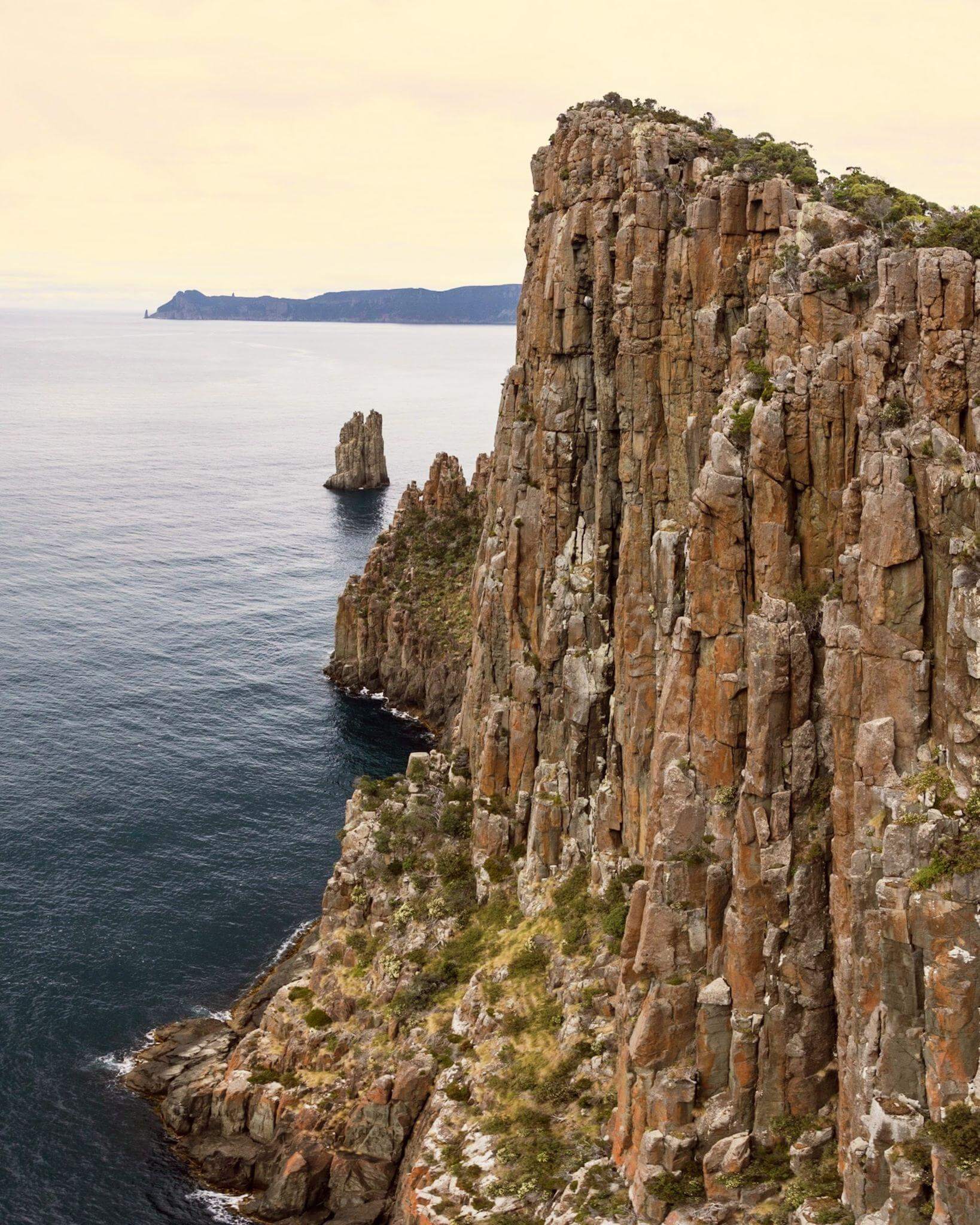 rugged dolorite cliffs overlooking an expansive calm ocean and glimpses of cape pillar in the distance