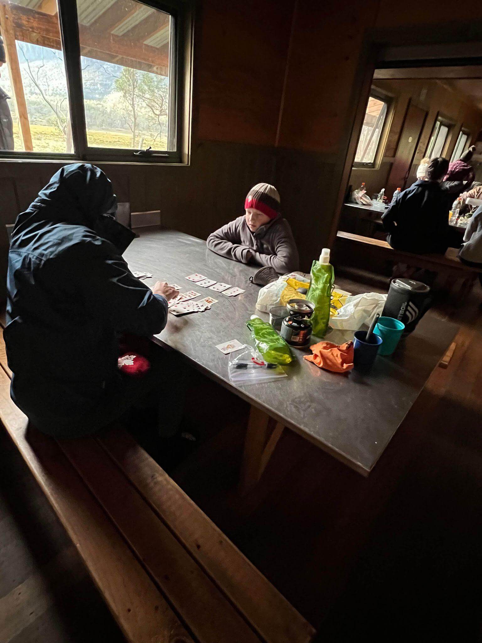Hikers relaxing inside mountain hut with beds and table showing comfortable accommodation option for multi-day walks