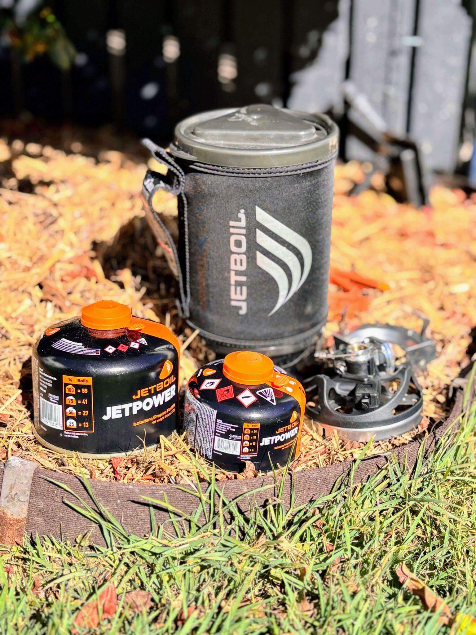 Jetboil camping stove system with gas canisters for multi-day hiking food preparation, showing compact cooking equipment essential for backpacking meals