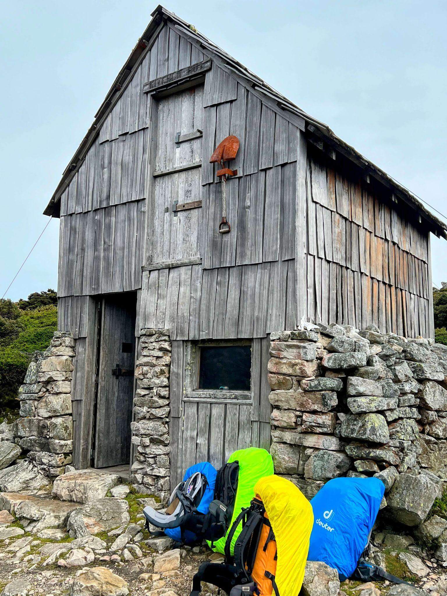 Weathered stone mountain hut with Deuter hiking backpacks showing proper pack rain cover use for hut to hut hiking